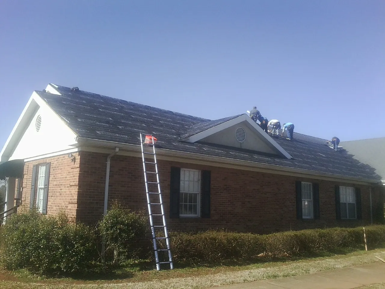 Crew tearing shingles off a brick ranch roof with a ladder set — Emergency Roof Repair work by our crew in Esopus