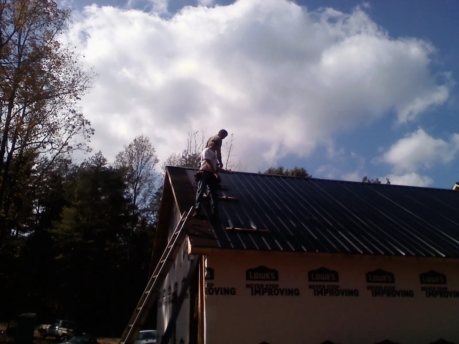Roofer fastening dark metal panels high against a cloudy sky, from a Roof Inspection job in Esopus